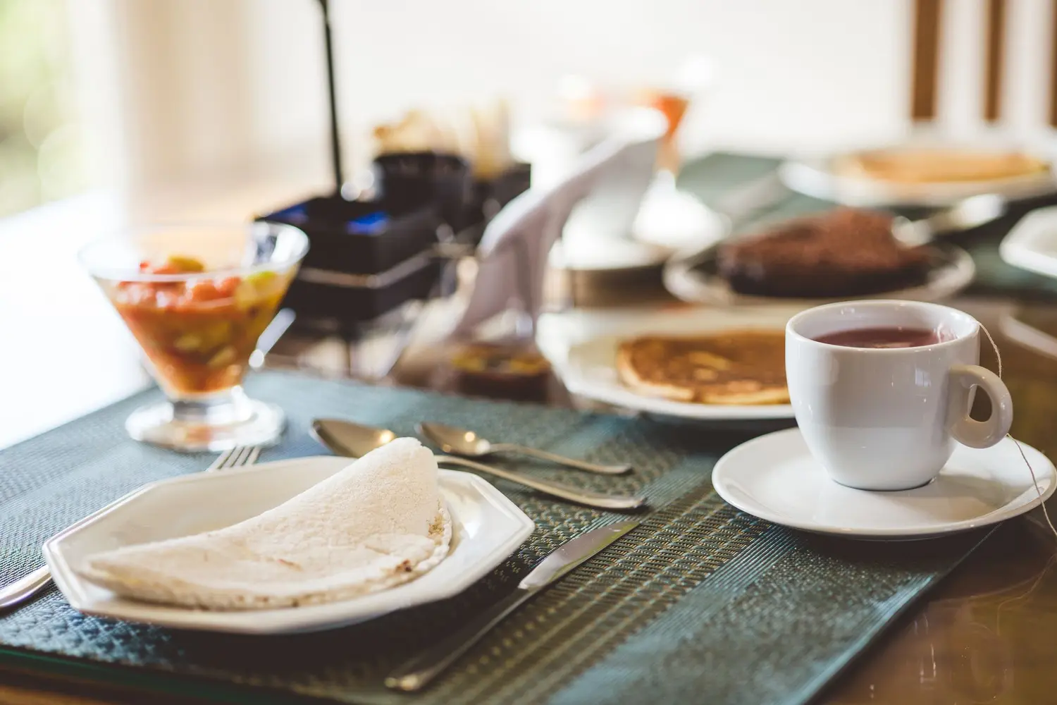 Mesa de café com tapioca dobrada no prato, xícara de café e salada de frutas