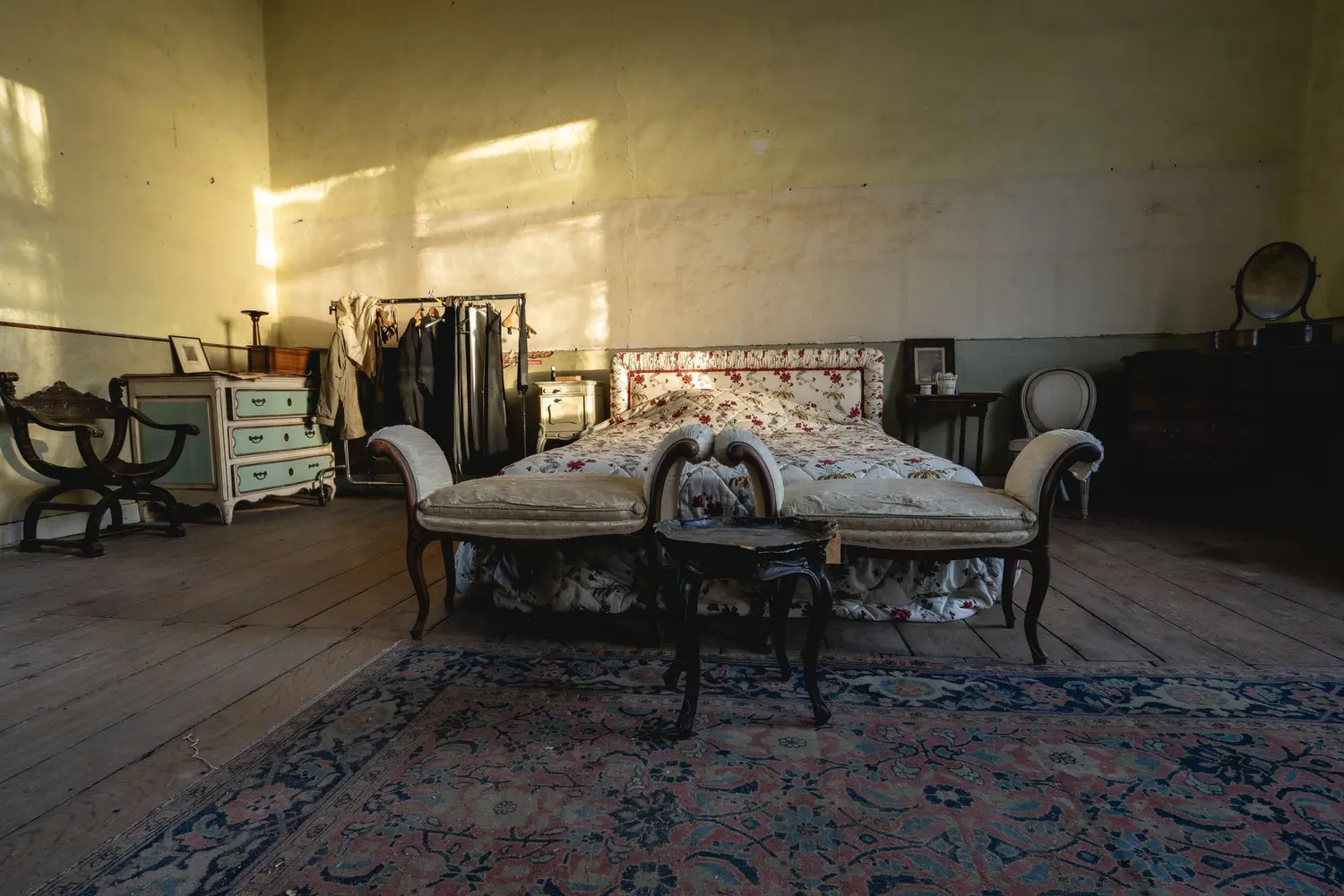 Quarto amplo com pé-direito alto, piso de tábua, tapete persa e cama antiga de cabeceira trabalhada